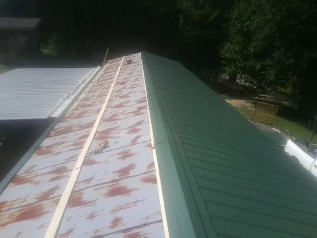 Old rusted panels beside newly installed green metal roofing — Wind Damage Roof Repair by Roofing Brothers in Norman