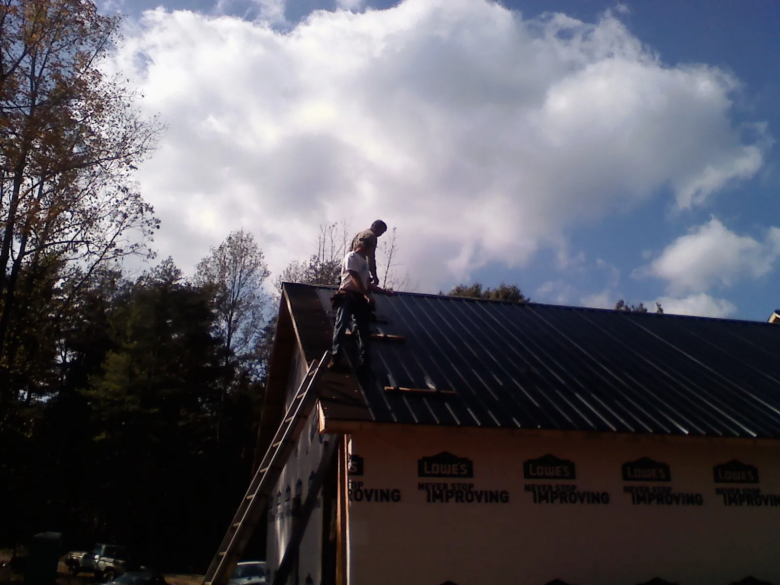 Roofer fastening dark metal panels high against a cloudy sky, from a Roof Inspection job in Norman