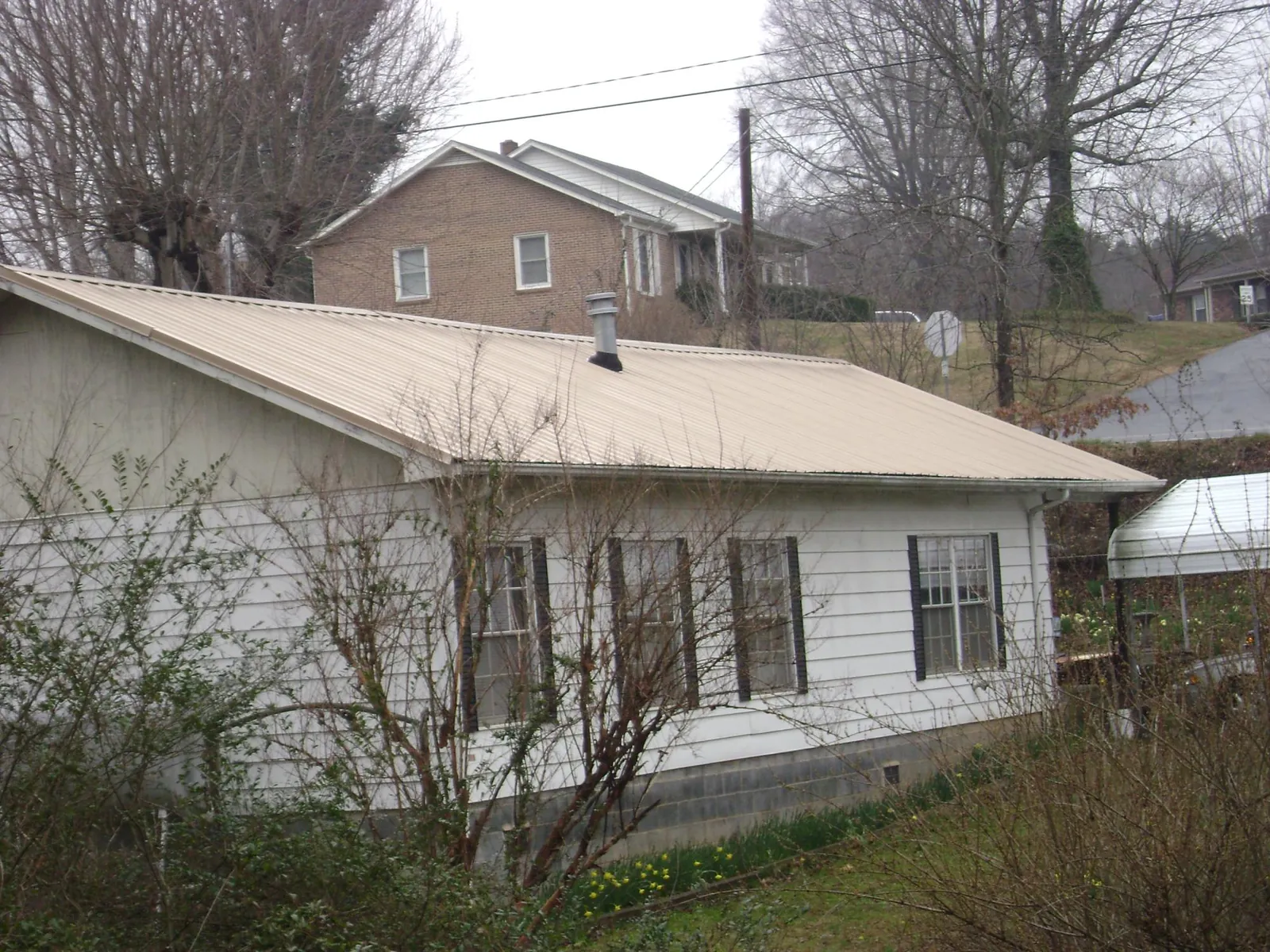 Tan metal roof on a white sided house set into a hillside — Commercial Roofing by Roofing Brothers in Norman
