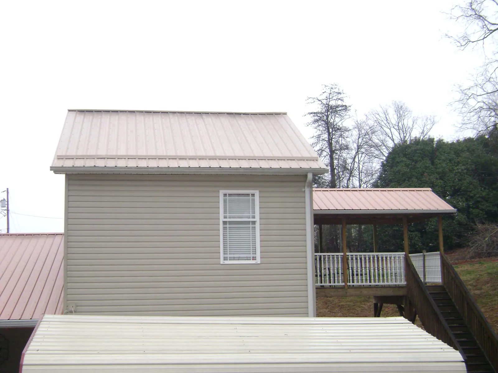 Tan metal roofs on a two story addition and attached porch, from a Roof Replacement job in Norman